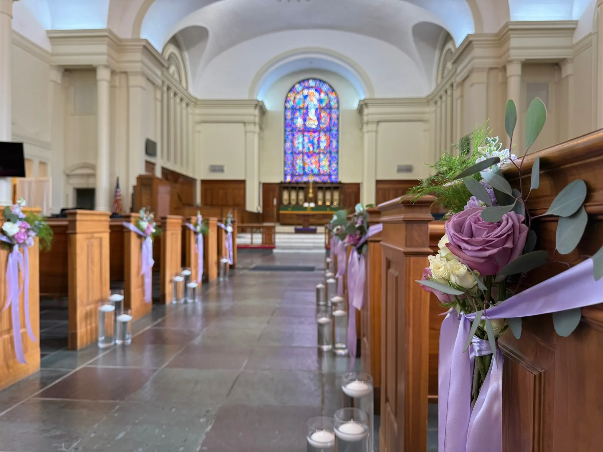 Church aisle decorated with lavender pew flowers and candles