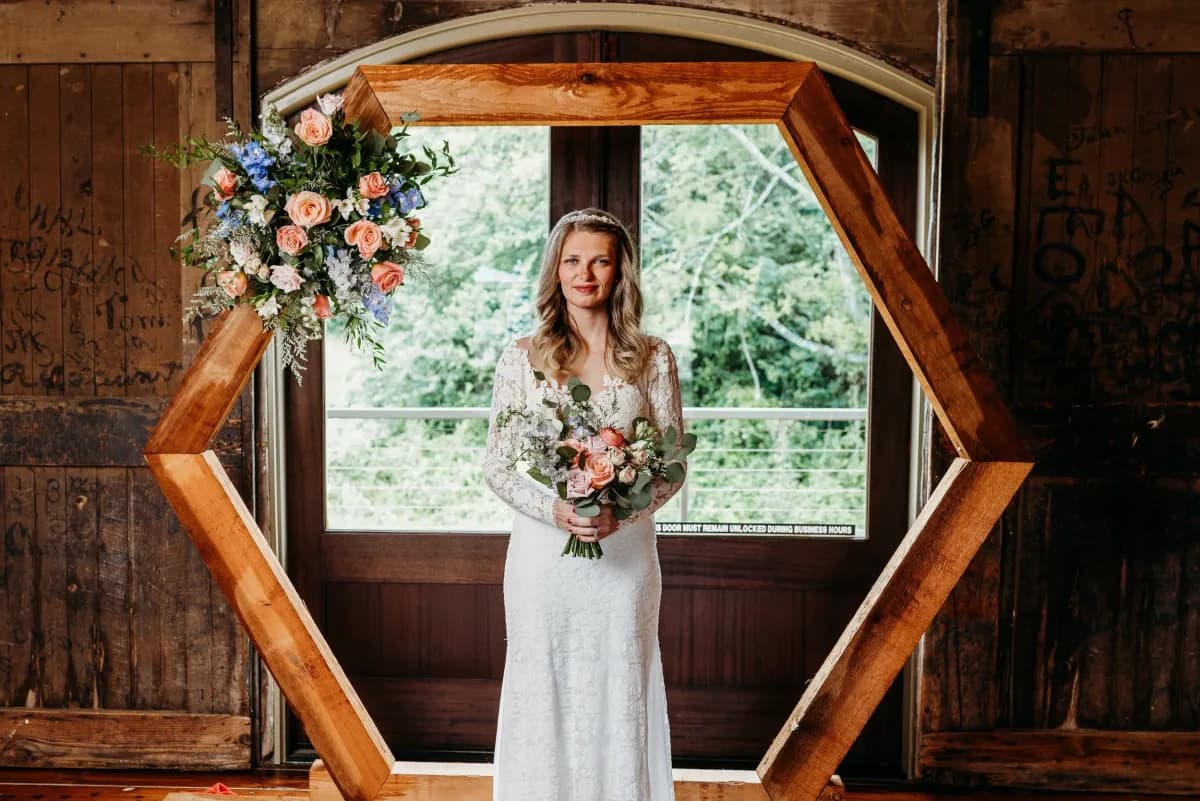 Bride standing in a hexagonal wooden arch adorned with coral and blue florals
